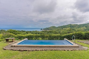 Una piscina rectangular con borde de piedra, rodeada por un césped cuidado y un seto.
