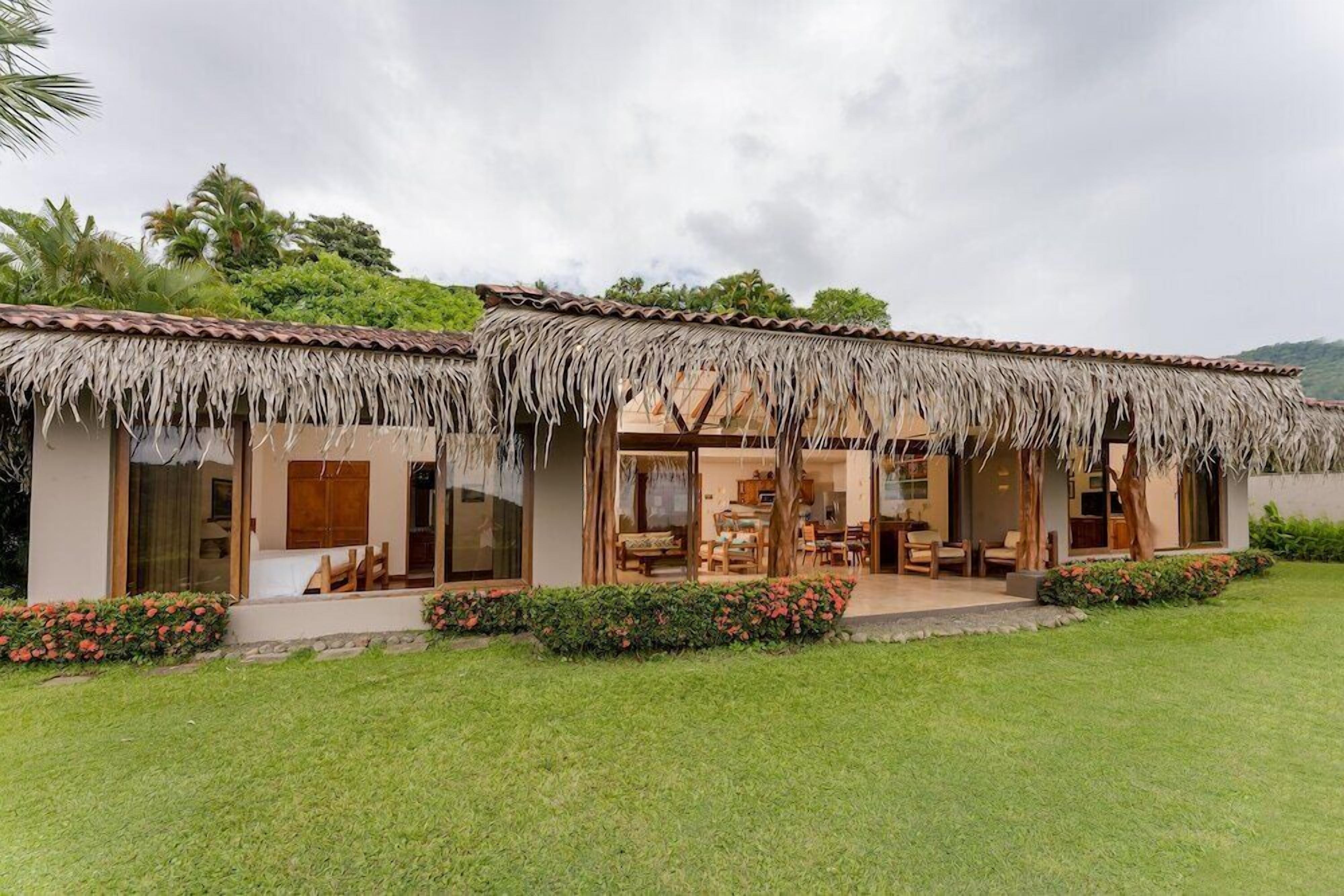 A two-story house with a thatched roof, large windows, and a well-maintained lawn.