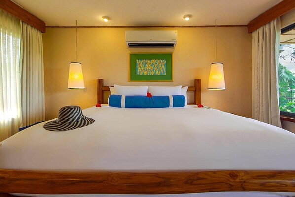 Una habitación de hotel con una cama grande, dos lámparas de noche, un equipo de aire acondicionado y una ventana con cortinas.