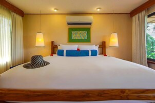 Una habitación de hotel con una cama grande, dos lámparas de noche, un equipo de aire acondicionado y una ventana con cortinas.