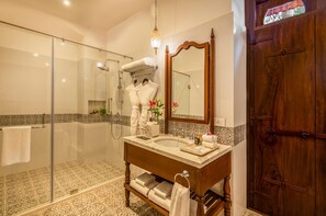 A bathroom with a glass shower enclosure, a wooden vanity with a marble countertop, and a large mirror. - Ama Stays And Trails Cardozo House (Candolim)