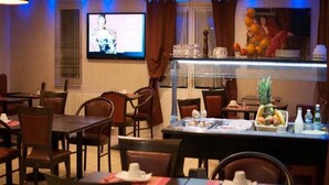 A restaurant with multiple tables and chairs, a television screen, and a fruit display. - Comfort Hotel Emerainville Marne-la-vallee (Emerainville)