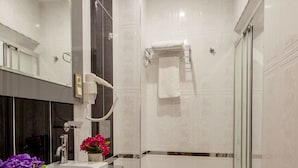 Moderni kylpyhuone, jossa on suuri peili, valkoinen pesuallas, wc ja suihkutila.