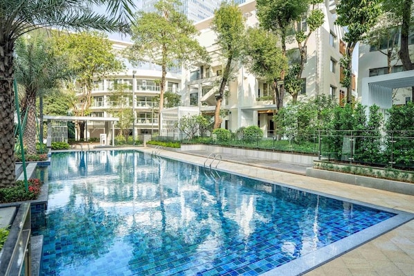 A swimming pool with a tiled edge, surrounded by greenery and modern buildings.