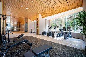 A gym with exercise equipment, a bench, and large windows offering a view of greenery. - CM Plus Service Apartment Shenzhen Taige (Shenzhen)