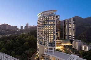 A multi-story hotel with a curved facade, surrounded by greenery and other buildings.