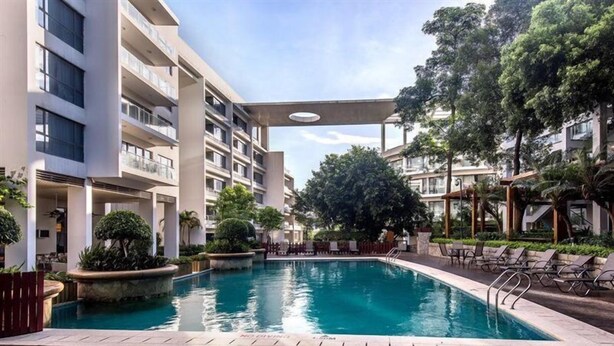 Una piscina rodeada de una terraza de madera, con un edificio de varios pisos al fondo.