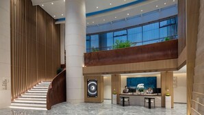 A modern hotel lobby with a curved staircase, a reception desk, and a large window overlooking the outdoors.