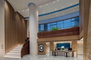 A modern hotel lobby with a curved staircase, a reception desk, and a large window overlooking the outdoors.