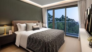 A modern bedroom with a large bed, a nightstand, a lamp, and a view of the outdoors through a large window.