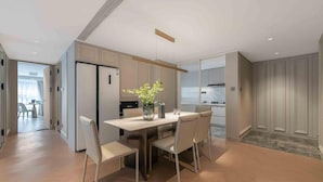 A modern kitchen with a dining area, featuring a wooden table and chairs, a vase with flowers, and a view into the adjacent living space.