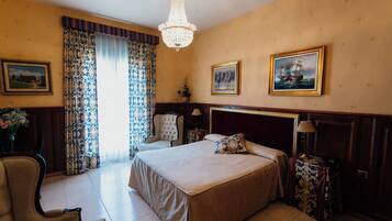 Habitación de hotel con una cama grande, una silla, un escritorio, una lámpara y una araña.