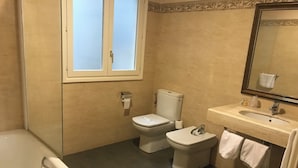 Un baño con bañera, dos inodoros, un lavamanos y un espejo.