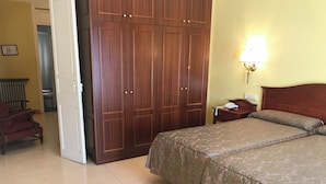 Habitación de hotel con cama, armario, mesita de noche con lámpara y una silla.