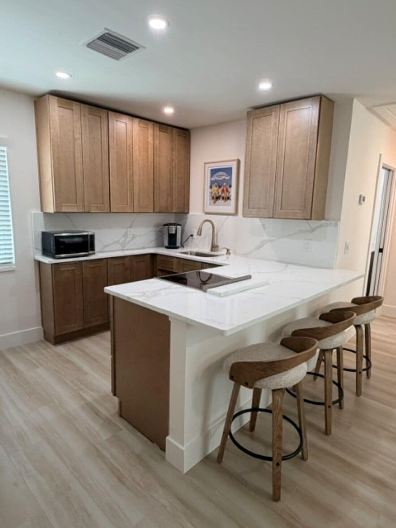 A modern kitchen with wooden cabinets, a white marble countertop, a built-in microwave, and a central island with bar stools.