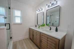 Un bagno moderno con doppio lavabo, due specchi, una doccia e una pianta in vaso.