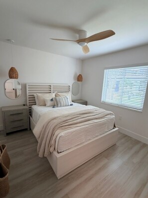 Una camera da letto con un letto, comodini, una ventola a soffitto, una finestra con tende e uno specchio.