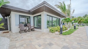 Ein modernes Haus mit Terrasse, zwei Adirondack-Stühlen und einem kleinen Garten.
