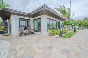 Una casa moderna con un patio, dos sillas Adirondack y un pequeño jardín.