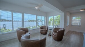 Ein geräumiges Zimmer mit großen Fenstern, einem Deckenventilator und Blick auf ein Gewässer.