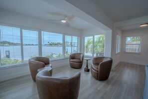 Amplia habitación con ventanas grandes, ventilador de techo y vista a un cuerpo de agua.