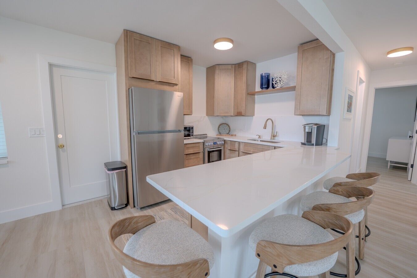 A modern kitchen with a central island, wooden cabinets, stainless steel appliances, and bar stools.