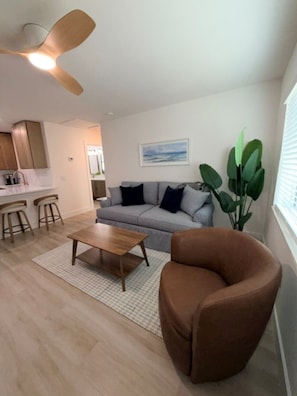 Een woonkamer met een bank, een salontafel, een bruine fauteuil, een plafondventilator en een plant.