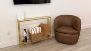 A room with a mounted television, a brown leather chair, and a gold-framed console table with decorative items. - 18 On the Bay Suite #6 (Indian Rocks Beach)