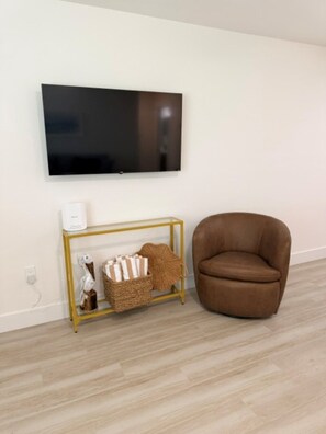 A room with a mounted television, a brown leather chair, and a gold-framed console table with decorative items. - 18 On the Bay Suite #6 (Indian Rocks Beach)