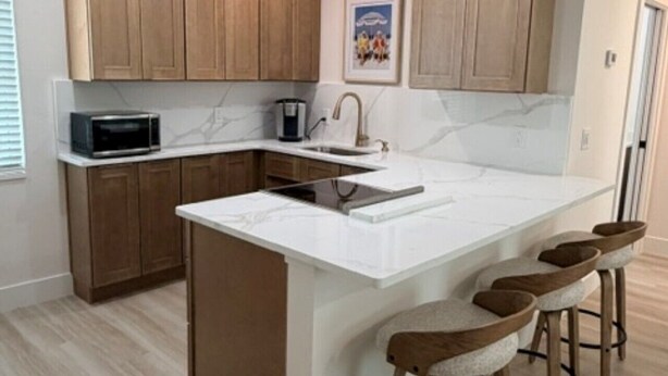 A modern kitchen with wooden cabinets, a white marble countertop, a built-in microwave, and a central island with bar stools. - 18 On the Bay Suite #6 (Indian Rocks Beach)