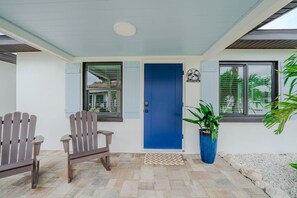 A covered porch with two Adirondack chairs, a blue door, and a potted plant. - 18 On the Bay Suite #5 (Indian Rocks Beach)