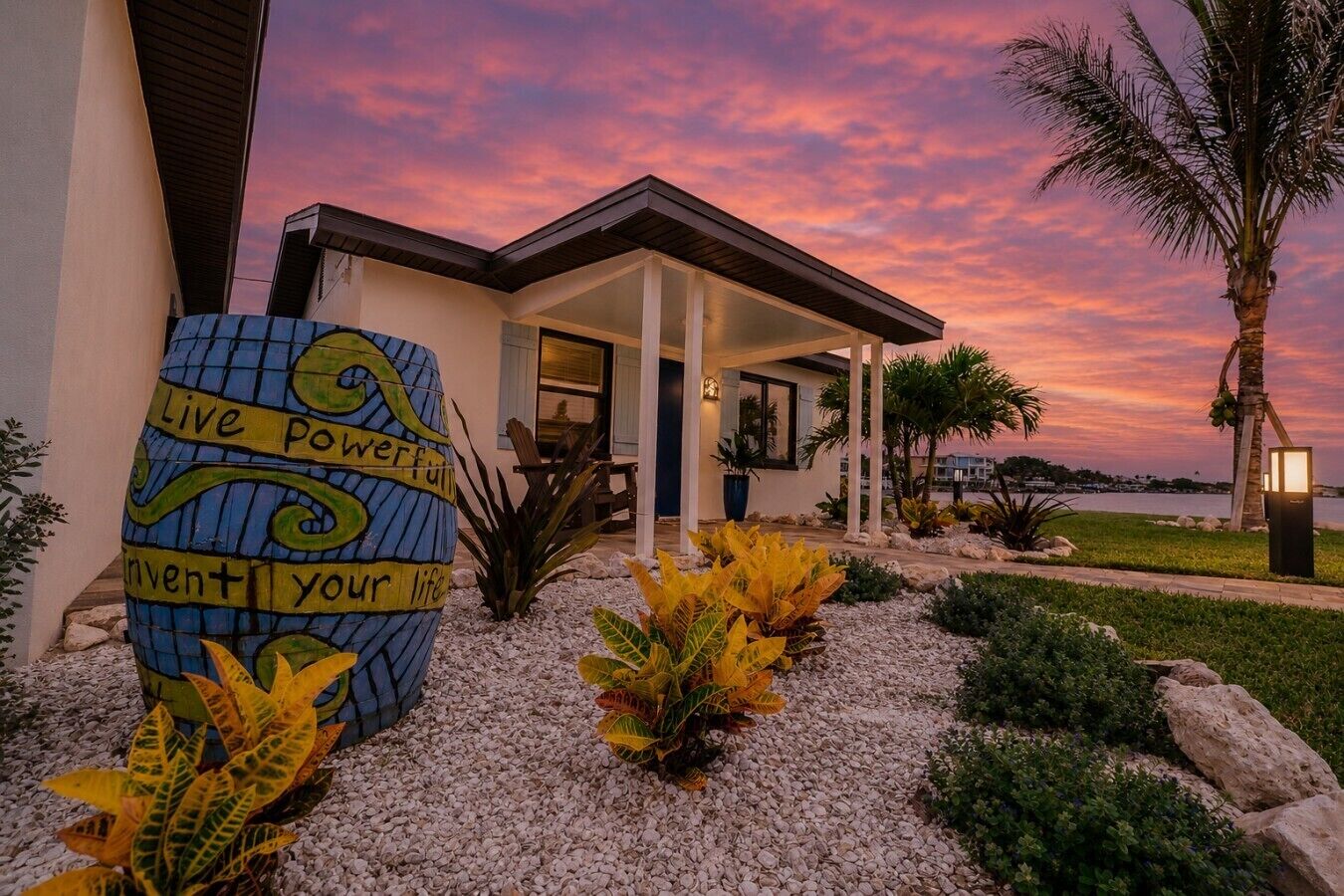 A modern house with a large decorative barrel and a view of the water at sunset.