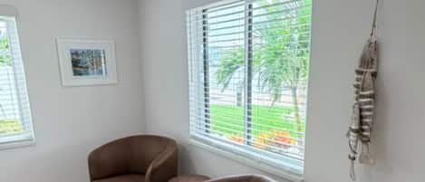 Quarto com duas poltronas marrons, janela com persianas, um quadro na parede e um objeto decorativo pendurado.