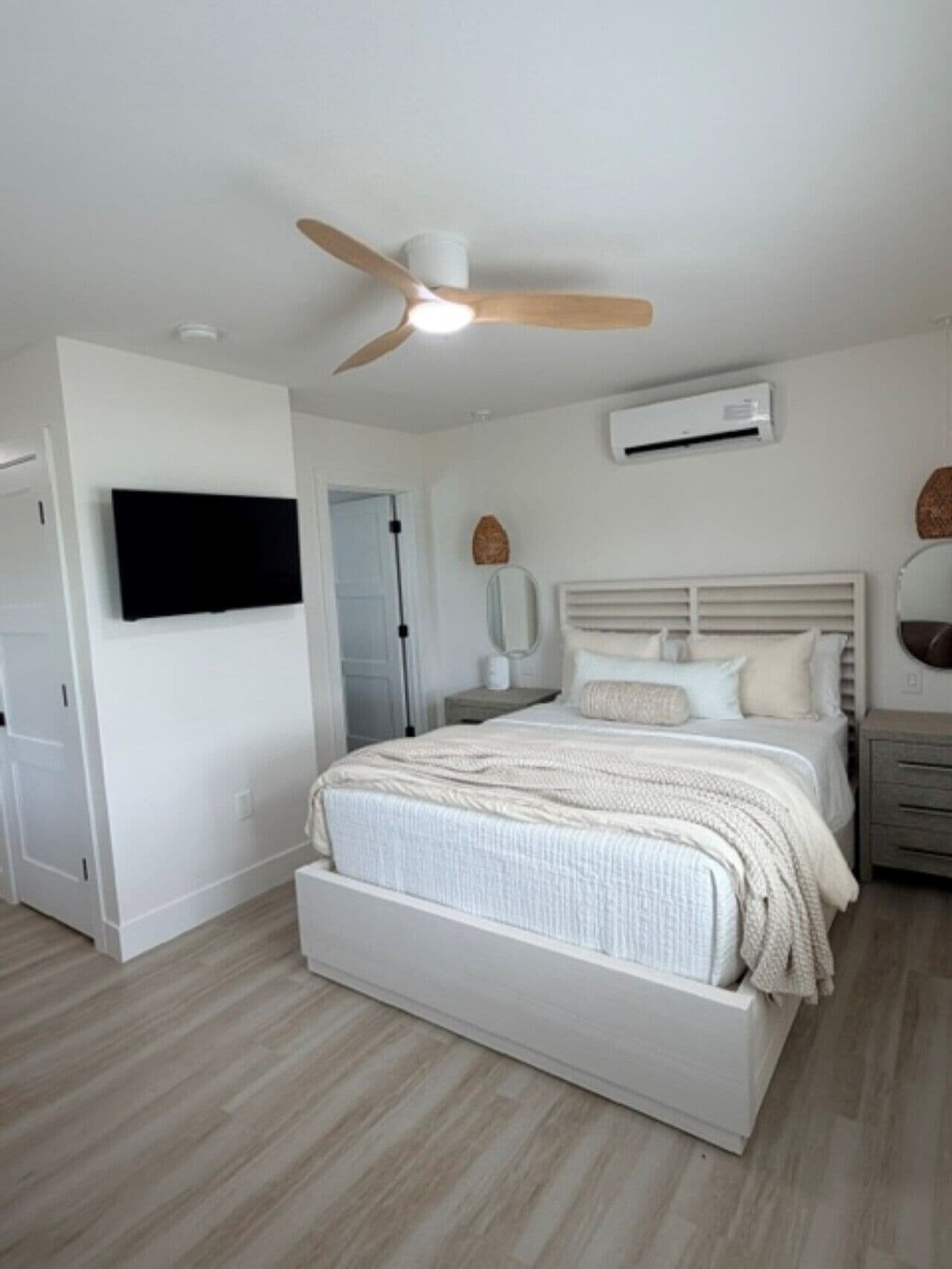 Een slaapkamer met een bed, een plafondventilator, een airconditioning en een aan de muur bevestigde televisie.