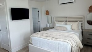 Une chambre à coucher comprenant un lit, un ventilateur de plafond, un appareil de climatisation et un téléviseur fixé au mur.