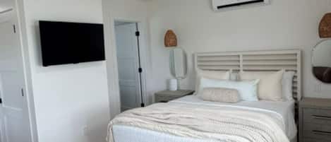 Une chambre à coucher comprenant un lit, un ventilateur de plafond, un appareil de climatisation et un téléviseur fixé au mur.