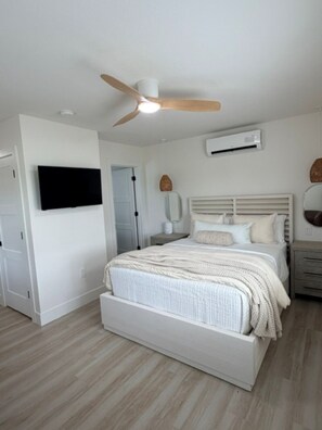 A bedroom with a bed, a ceiling fan, an air conditioning unit, and a television mounted on the wall. - 18 On the Bay Suite #5 (Indian Rocks Beach)