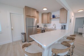A modern kitchen with a central island, wooden cabinets, stainless steel appliances, and bar stools. - 18 On the Bay Private Resort (Indian Rocks Beach)