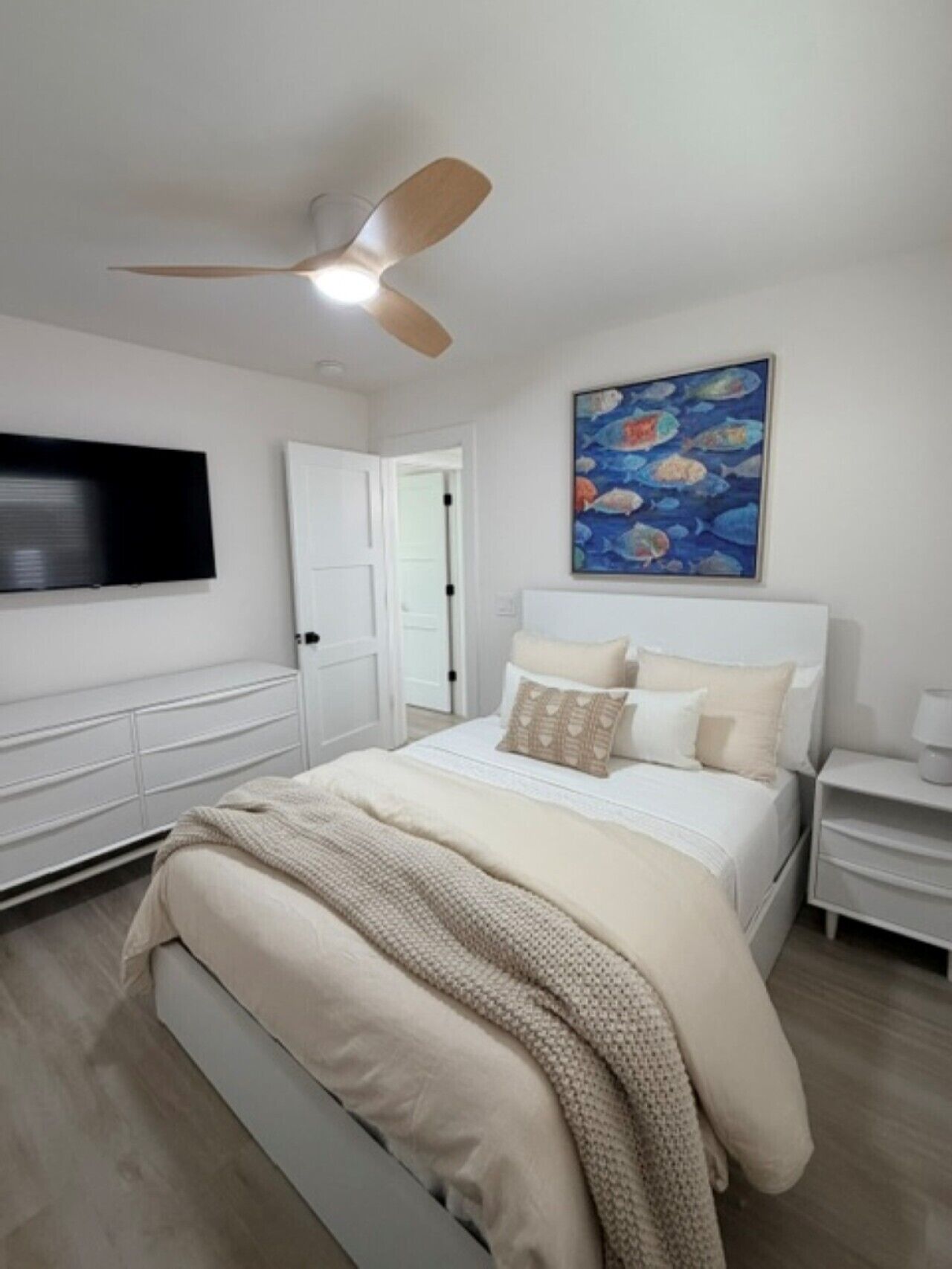 A bedroom with a bed, a ceiling fan, a painting, a TV, and a nightstand.