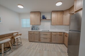 A modern kitchen with wooden cabinets, a stainless steel refrigerator, and a bar area with stools. - 18 On the Bay Suite #2 (Indian Rocks Beach)