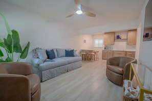 A living room with a sofa, a brown armchair, a ceiling fan, and a kitchen area with wooden cabinets and a dining table. - 18 On the Bay Suite #2 (Indian Rocks Beach)