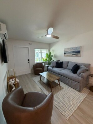A living room with a sofa, a coffee table, a brown leather chair, a ceiling fan, and a window with a view of the outdoors. - 18 On the Bay Suite #2 (Indian Rocks Beach)