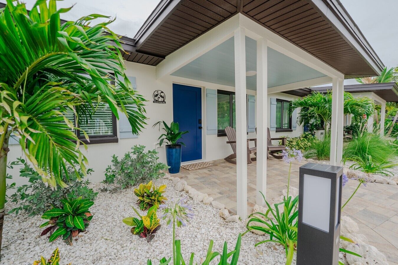 Een modern huis met een overdekt terras, een blauwe deur en verschillende planten.
