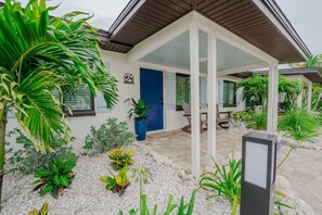 Een modern huis met een overdekt terras, een blauwe deur en verschillende planten.