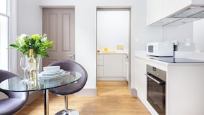 Una cocina moderna con armarios blancos, un microondas y un horno. Hay una mesa de vidrio con sillas y un jarrón con flores.