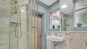 Un baño moderno con ducha de vidrio, un lavamanos blanco y un espejo encima.