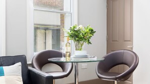 Una habitación moderna con una mesa de vidrio, dos sillones de cuero, un florero con flores y una botella de vino.