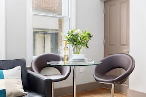 Quarto moderno com mesa de vidro, duas poltronas de couro, um vaso com flores e uma garrafa de vinho.