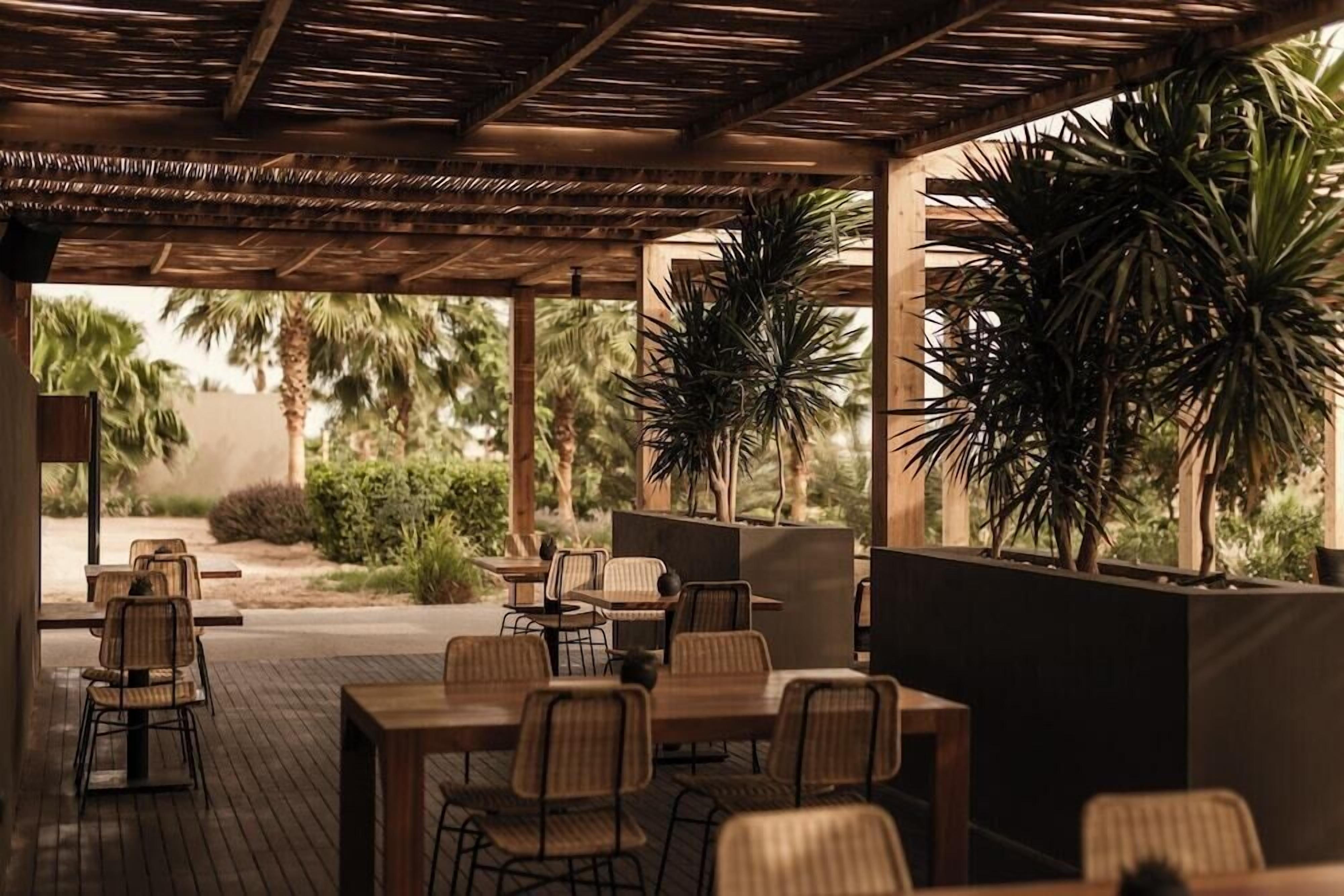 An outdoor patio area with tables and chairs, surrounded by plants and palm trees.