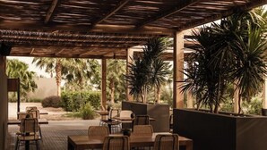 An outdoor patio area with tables and chairs, surrounded by plants and palm trees. - Casa Cook El Gouna (El Gouna)